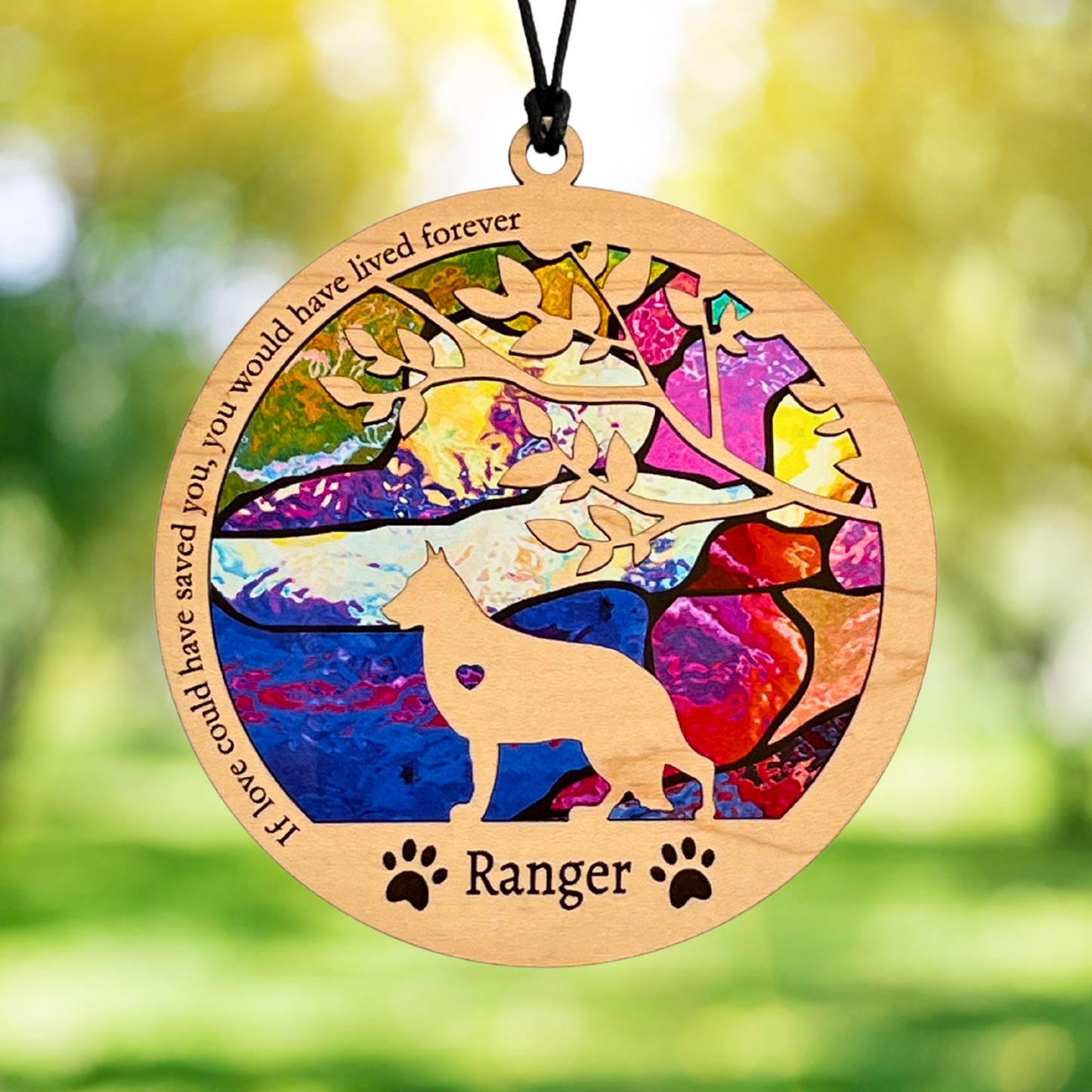 Wooden memorial suncatcher with colorful design and text, featuring a german shepherd silhouette, against a blurred natural background.